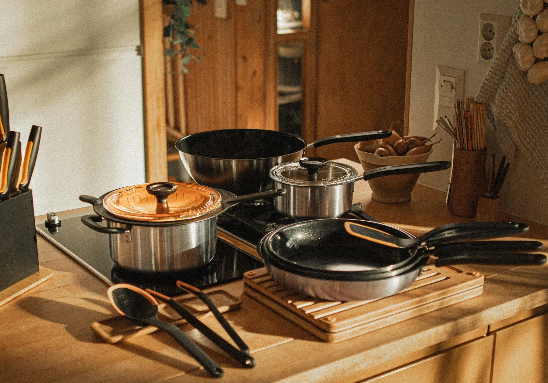 Fiskars_Functional_Form_DavidssonsJarn Köksredskap från Fiskars Functional Form uppställda på en köksbänk, med kastruller, stekpannor och köksverktyg med svarta och orangea handtag.